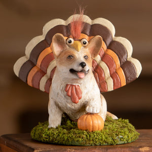 A charming white tommy corgi figurine dressed as a turkey with orange comb sitting on moss by a pumpkin bethany lowe