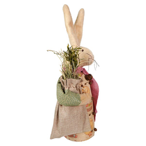 A charming beige fabric attire white bunny wearing a patchwork apron and scarf holding a sack of dried greenery