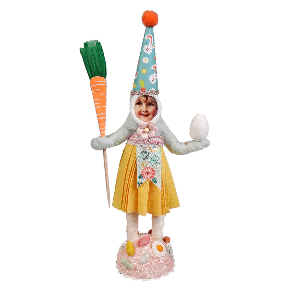 Easter girl handcrafted folk art figurine in yellow skirt and gray top with teal bunny hat holding carrot pick and egg