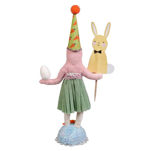 Handcrafted pink paper-mâché easter girl figure wearing green carrot hat holding white egg and yellow bunny pick