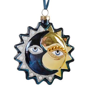 A glossy eclipse glass ornament by cody foster with deep blue and gold crescent moon and sun design with glittery eyes
