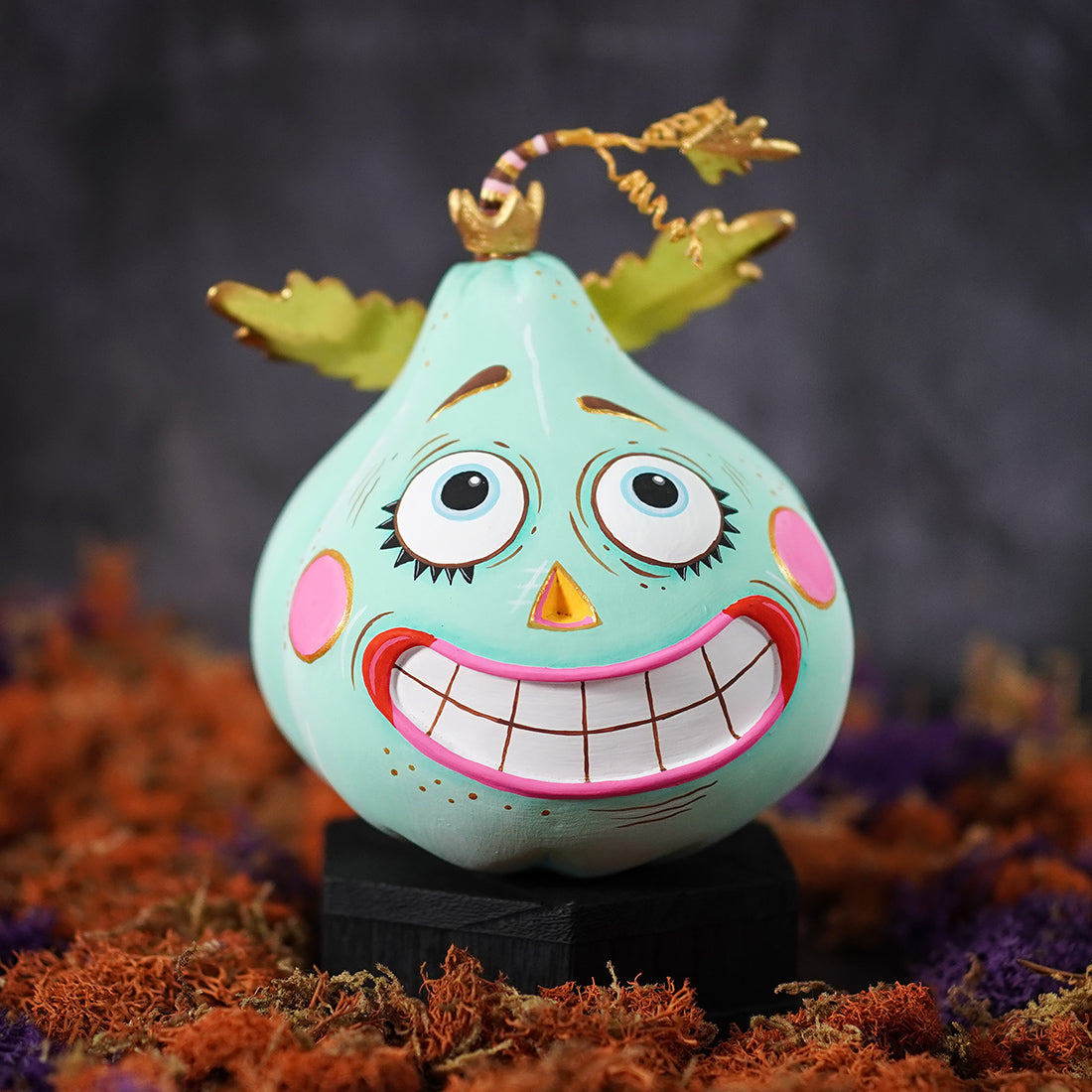 A turquoise hand painted pumpkin pixie display with ecstatic seafoam green color and a cartoonish grin