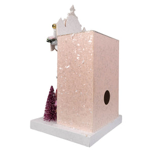 A pink glittery birdhouse with a white roof from ellen’s shoe shoppe by cody foster with light cord detail