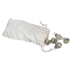 A white muslin bag set spilling embossed antique silver mercury glass ornaments with textured faceted surfaces