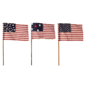 Three vintage-style American flags on wooden poles displayed side by side.