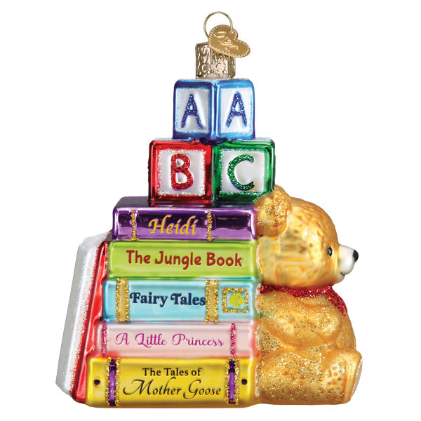 A golden glittery teddy bear with a red scarf sits beside colorful glass books and blocks in a book club ornament