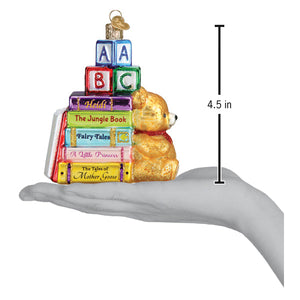 Golden glass teddy bear with red scarf sits beside colorful books and blocks with key in favorite children’s book club ornament lighted decor