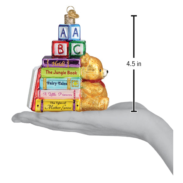 Golden glass teddy bear with red scarf sits beside colorful books and blocks with key in favorite children’s book club ornament lighted decor