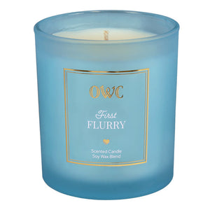 A light blue frosted glass candle jar with a gold-trimmed label featuring owc first flurry scent from creative co-op candle set