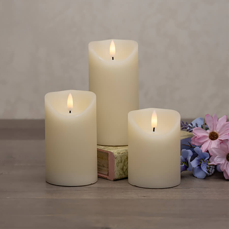 Three lit white pillar candles with glowing flames.