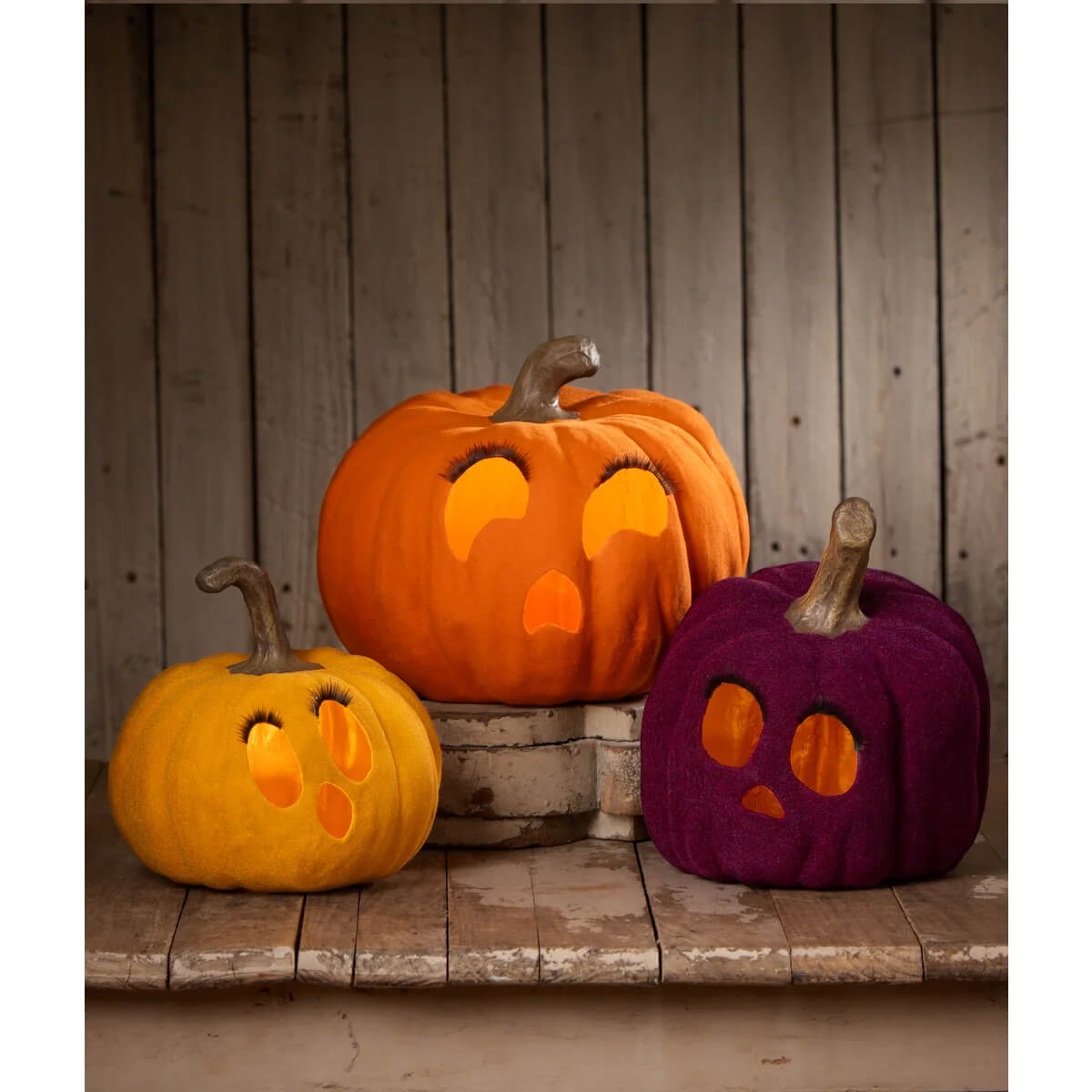 Three illuminated bethany lowe flocked mustard jol tealight pumpkins with orange and purple plush embroidered faces