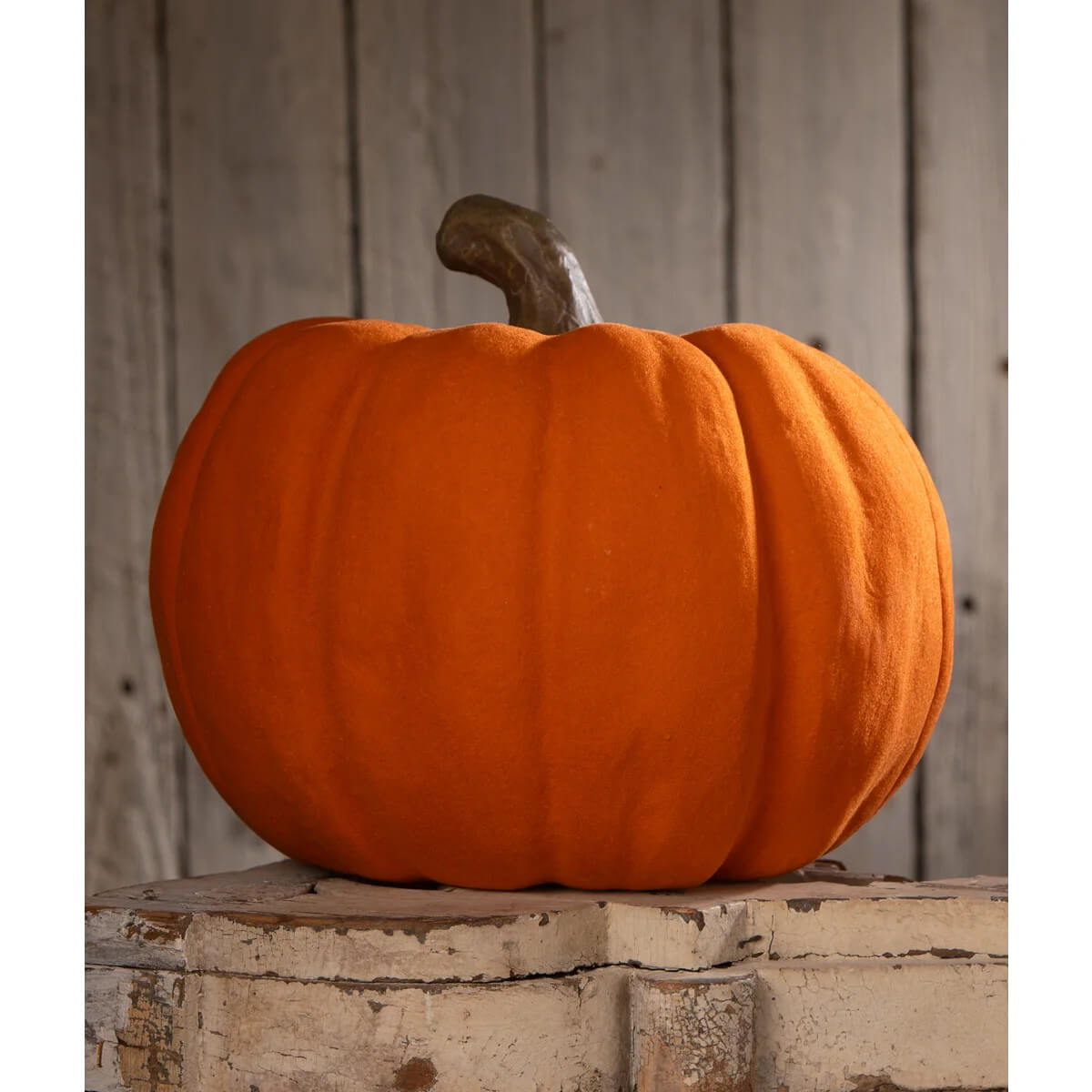 A bethany lowe flocked orange jol with a plush fabric surface and dark brown stem on a white wooden block
