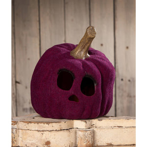 A plush deep purple flocked purple jol pumpkin with a carved skull face and a rustic wooden stem by bethany lowe design