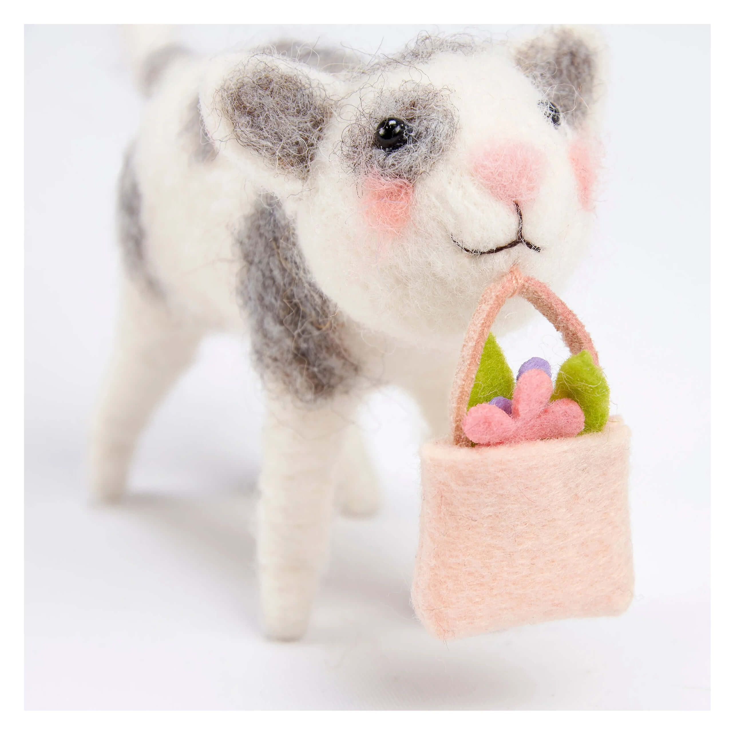 A charming white and gray felt cat critter holding a peach felt basket with flowers perfect for easter and spring tabletop decor