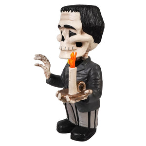 A black-and-white franken skelly figurine holding a lit candle on a tray dressed in a dark suit and striped pants