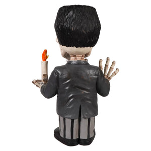 Black-haired franken skelly figure in dark gray suit and striped pants holding an orange flame candle