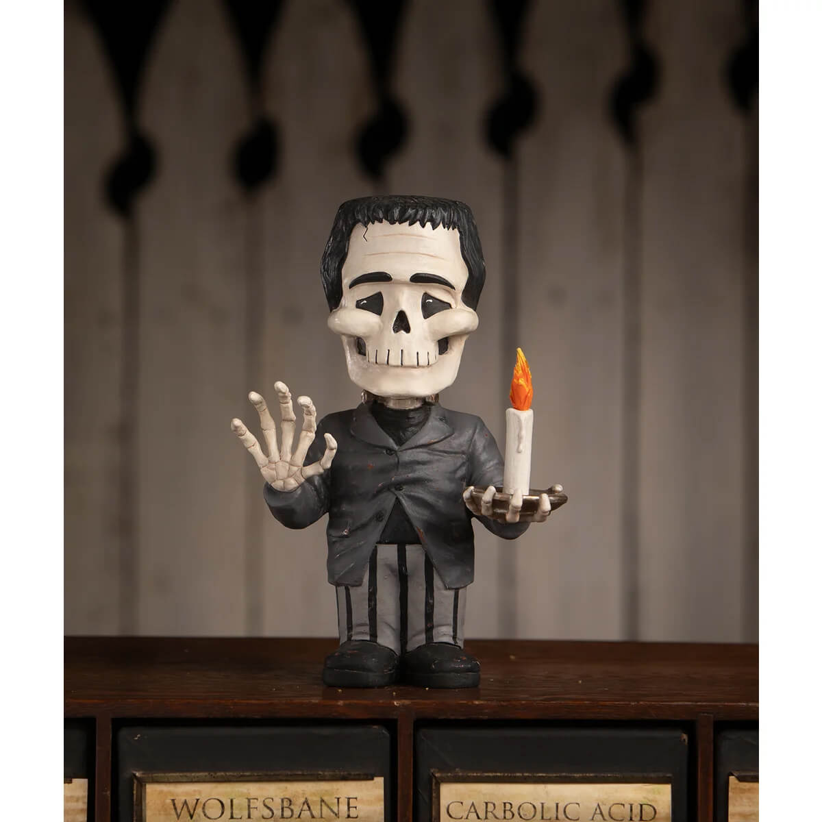 Franken skelly figurine with black hair white skull face and gray suit holding a lit candle for spooky decor