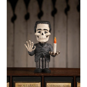 Franken skelly figurine with black hair white skull face and gray suit holding a lit candle for spooky decor