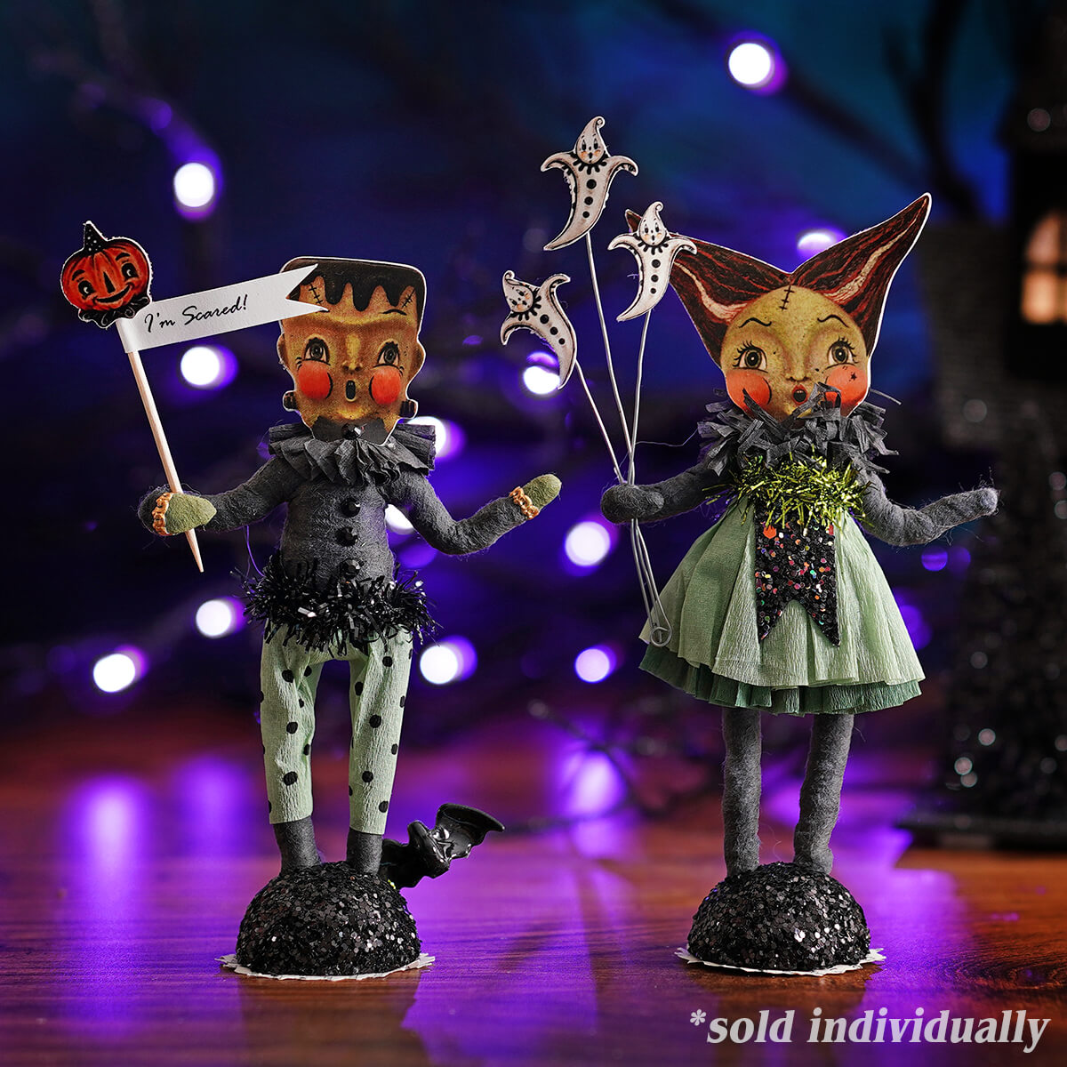 Two halloween-themed paper doll figurines featuring a frankenstein in black polka-dot outfit and a glittery green dress