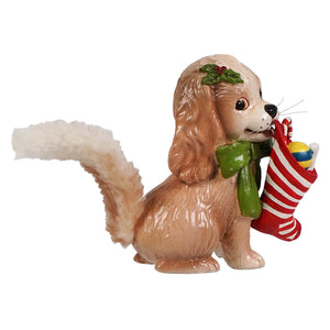 A tan cavalier king charles spaniel figurine with white tail wearing holly wreath and scarf holding christmas stocking by bethany lowe