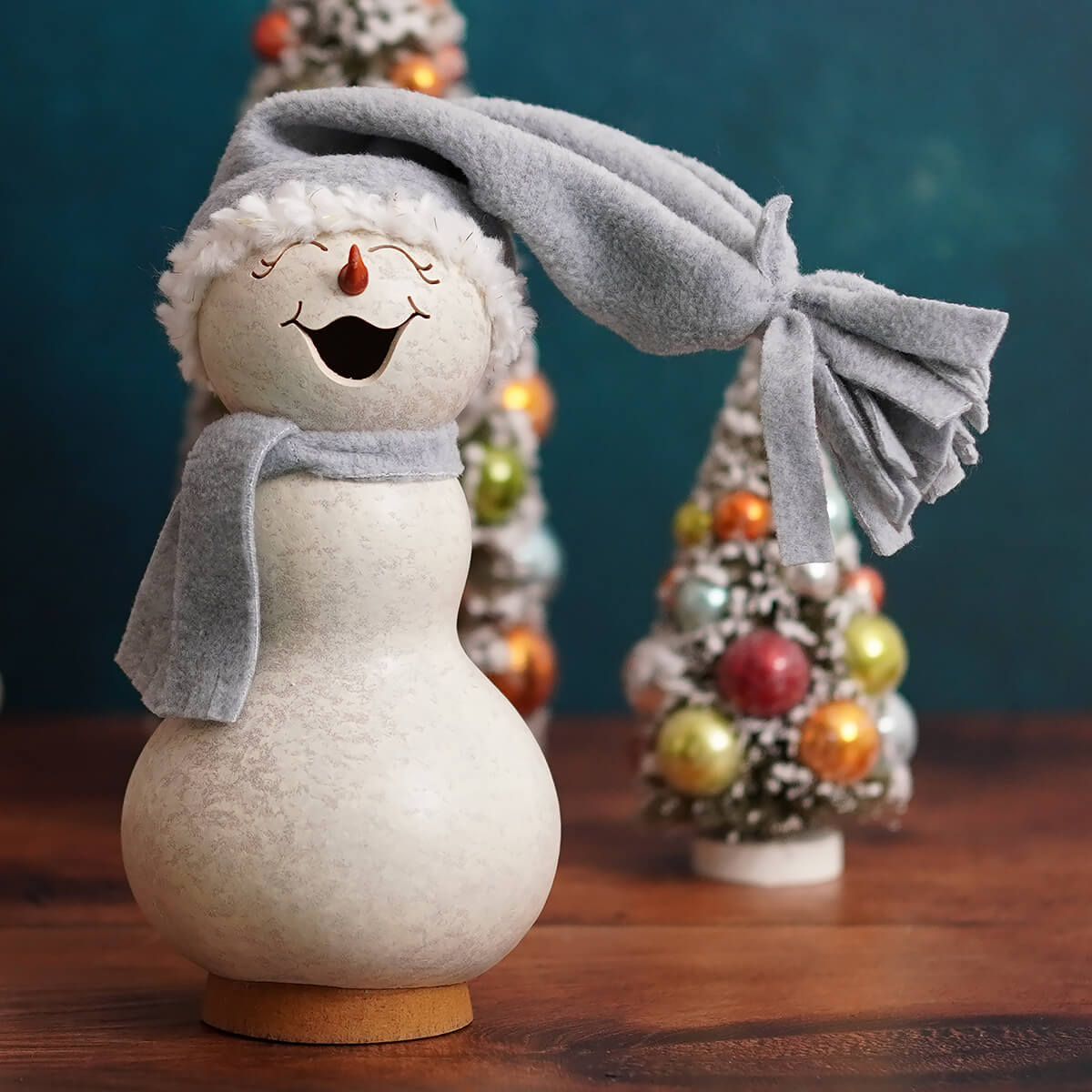 A cheerful white frostworth small girl snowman gourd with textured surface wearing gray fuzzy hat and scarf, perfect for snowman gourds collection