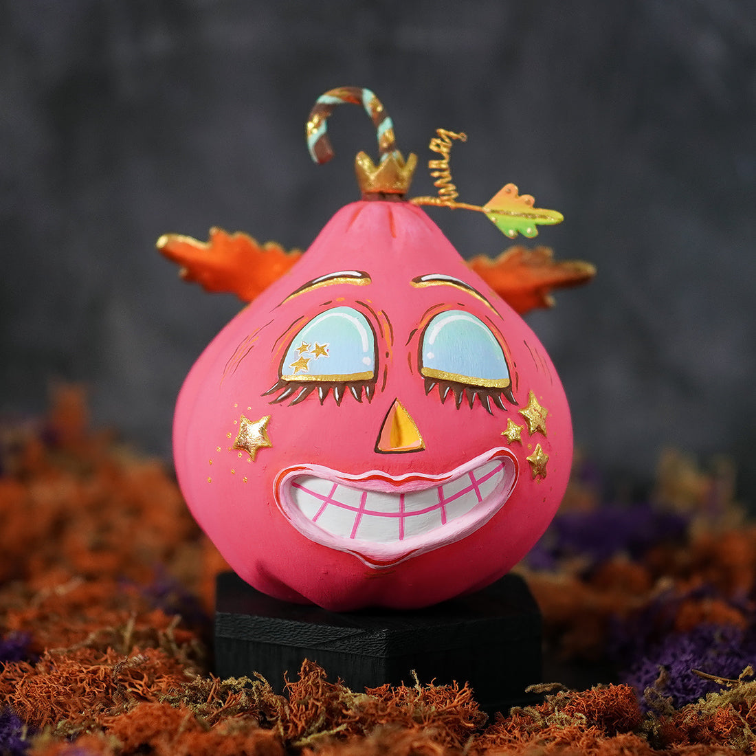 A vibrant pink hand-painted fulfilled hot pink pixie pumpkin figurine with gold-trimmed eyes lips crown and candy cane