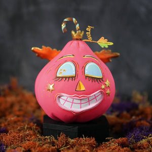 A vibrant pink hand-painted fulfilled hot pink pixie pumpkin figurine with gold-trimmed eyes lips crown and candy cane