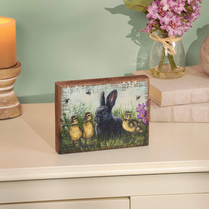 Decorative wooden box featuring artwork of a black rabbit with baby chicks in a garden setting.