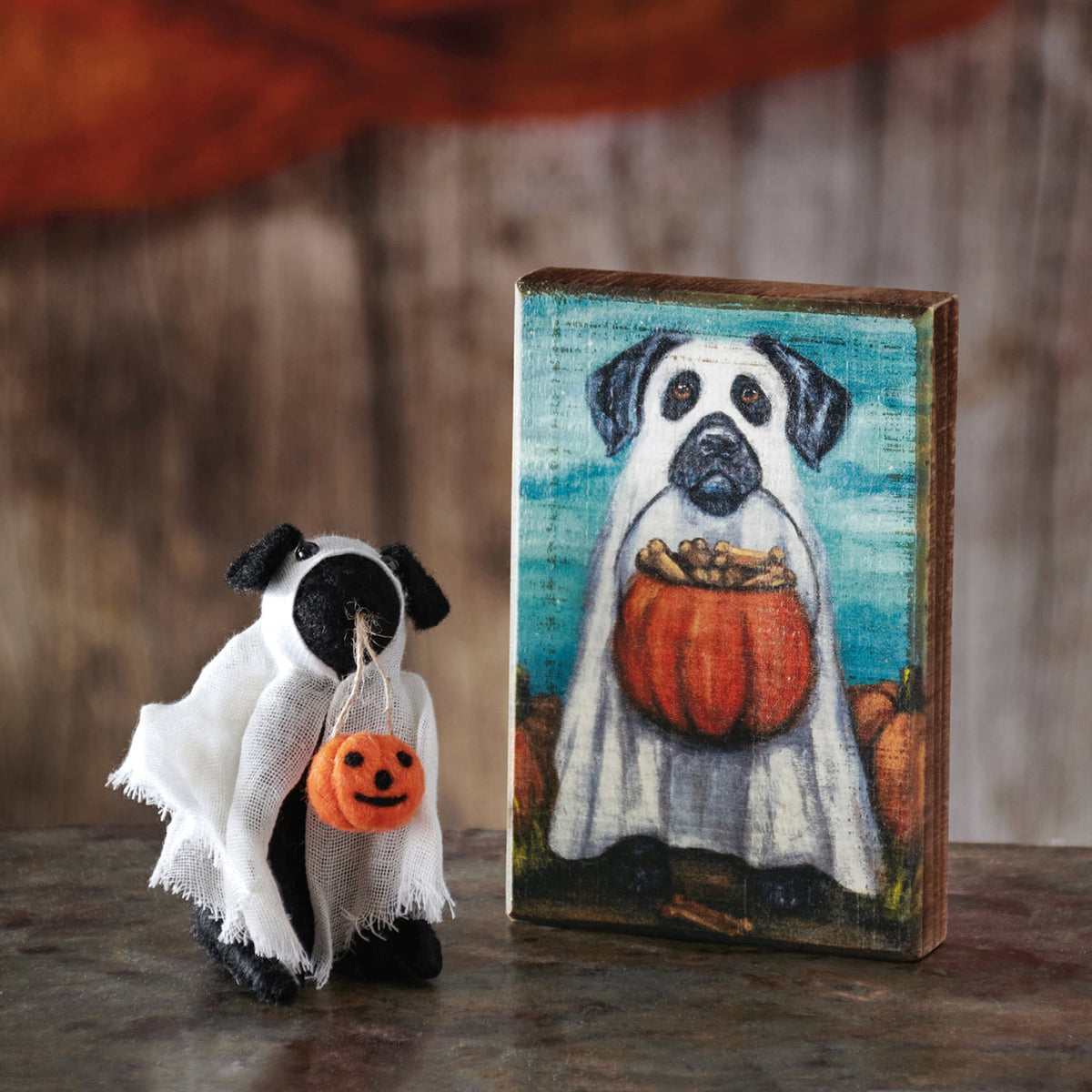 A plush black and white pug ghost critter holding an orange pumpkin bag from kathy’s halloween collection