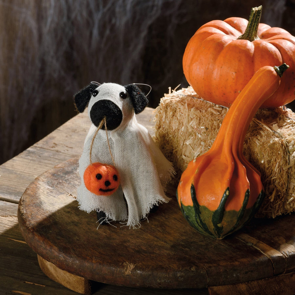 White fabric ghost dog critter with black ears and nose holding orange pumpkin from kathys halloween collection