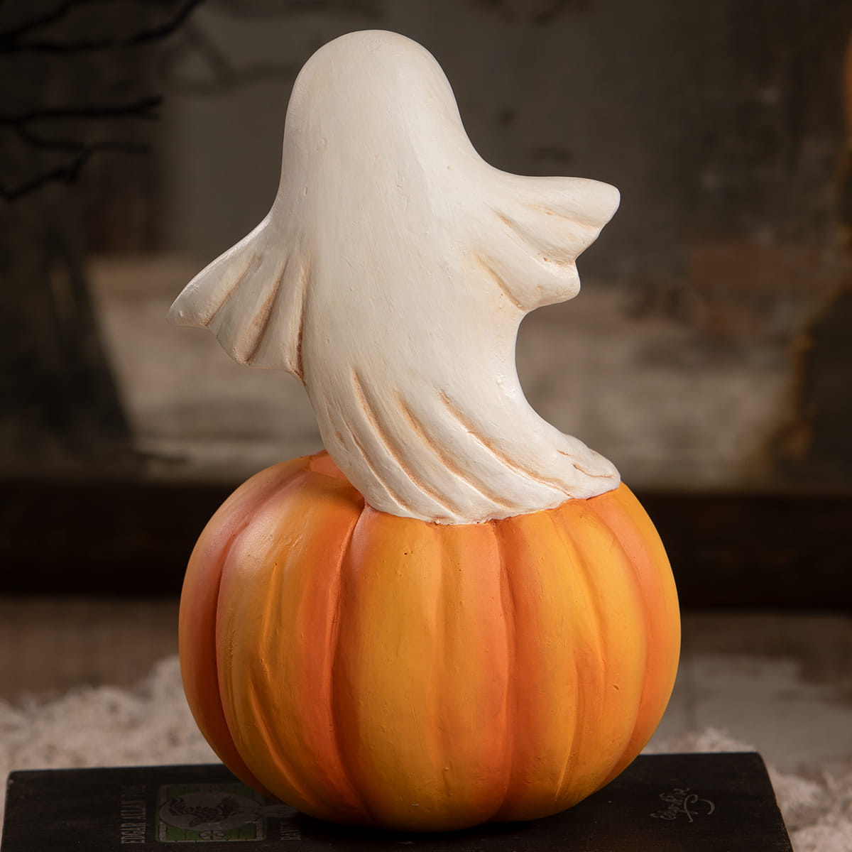 A white ghost figurine halloween ghost figures decor perched on a ribbed orange jack o lantern pumpkin
