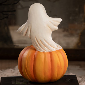 A white ghost figurine halloween ghost figures decor perched on a ribbed orange jack o lantern pumpkin