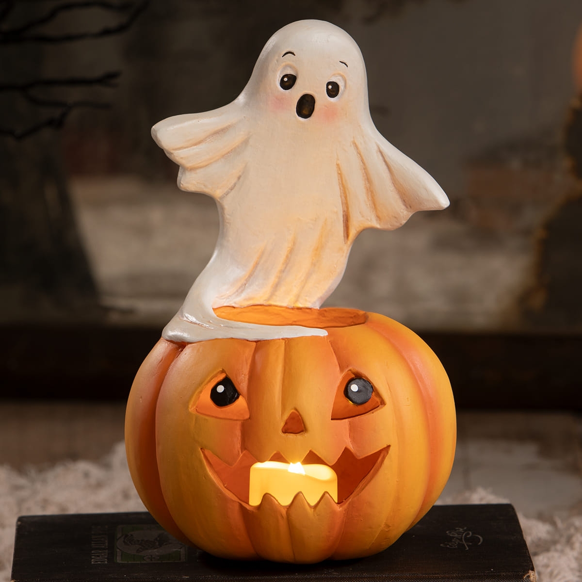 A whimsical orange jack o lantern with a glowing candle topped by a translucent white ghost figurine for halloween ghost figures decor and ornaments
