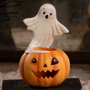 A white plastic ghost figure with black eyes and smile sits on an orange jack o lantern halloween ghost figures decor