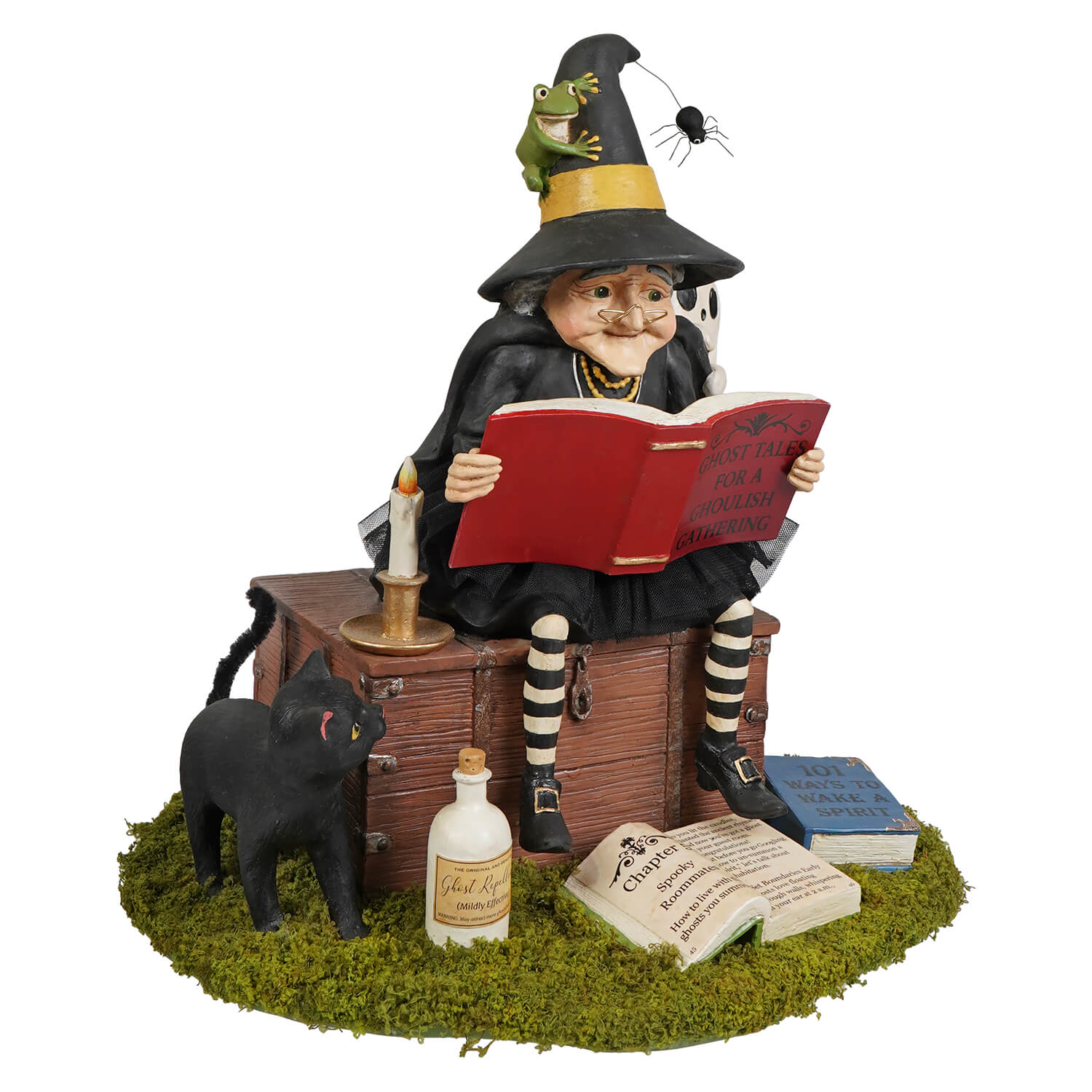 A whimsical ghost stories witch figurine with black hat and striped stockings sitting on wooden chest reading a red book