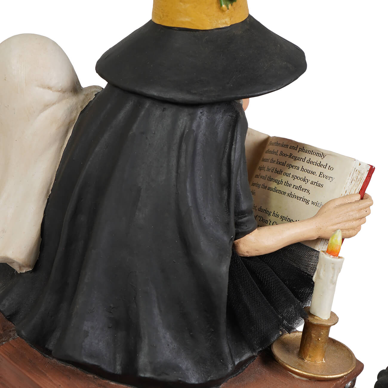 A black witch figurine with a yellow hat and white angel wings holding an open book beside a candle for halloween witches decor