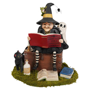 A whimsical halloween witch figurine with black and yellow hat reading ghost stories surrounded by witch decor accessories
