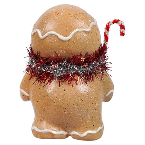 A festive gingerbread boy figurine with white icing and a red silver tinsel scarf holding a candy cane spreading holiday cheer