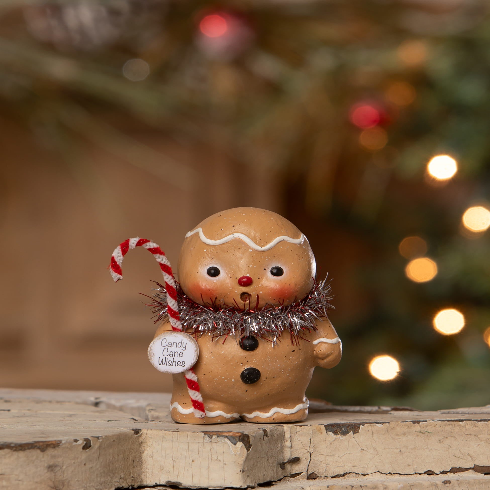 A charming tan gingerbread boy figurine with white icing and silver tinsel scarf spreading holiday cheer in gingerbread village decor