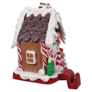 A festive gingerbread house stocking holder with a brown textured body, purple glitter roof, and candy cane pillars for christmas stockings