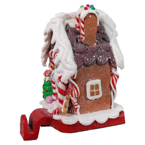 A festive gingerbread house stocking holder with glittery brown facade white icing roof candy cane decorations and sprinkles