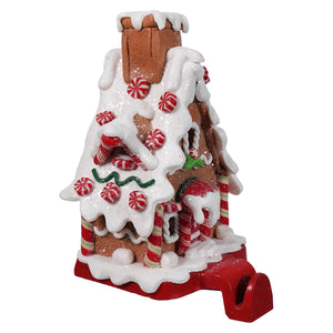 A festive gingerbread candy house stocking holder decorated with white icing red peppermint candies and candy canes