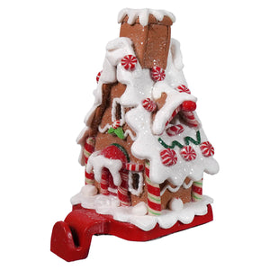 A festive gingerbread candy house stocking holder with brown glittery facade white icing and peppermint candy details
