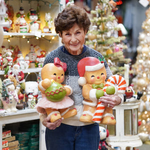 A cheerful woman holds two large vintage-style gingerbread figures from bethany lowe designs gingerbread joy collection