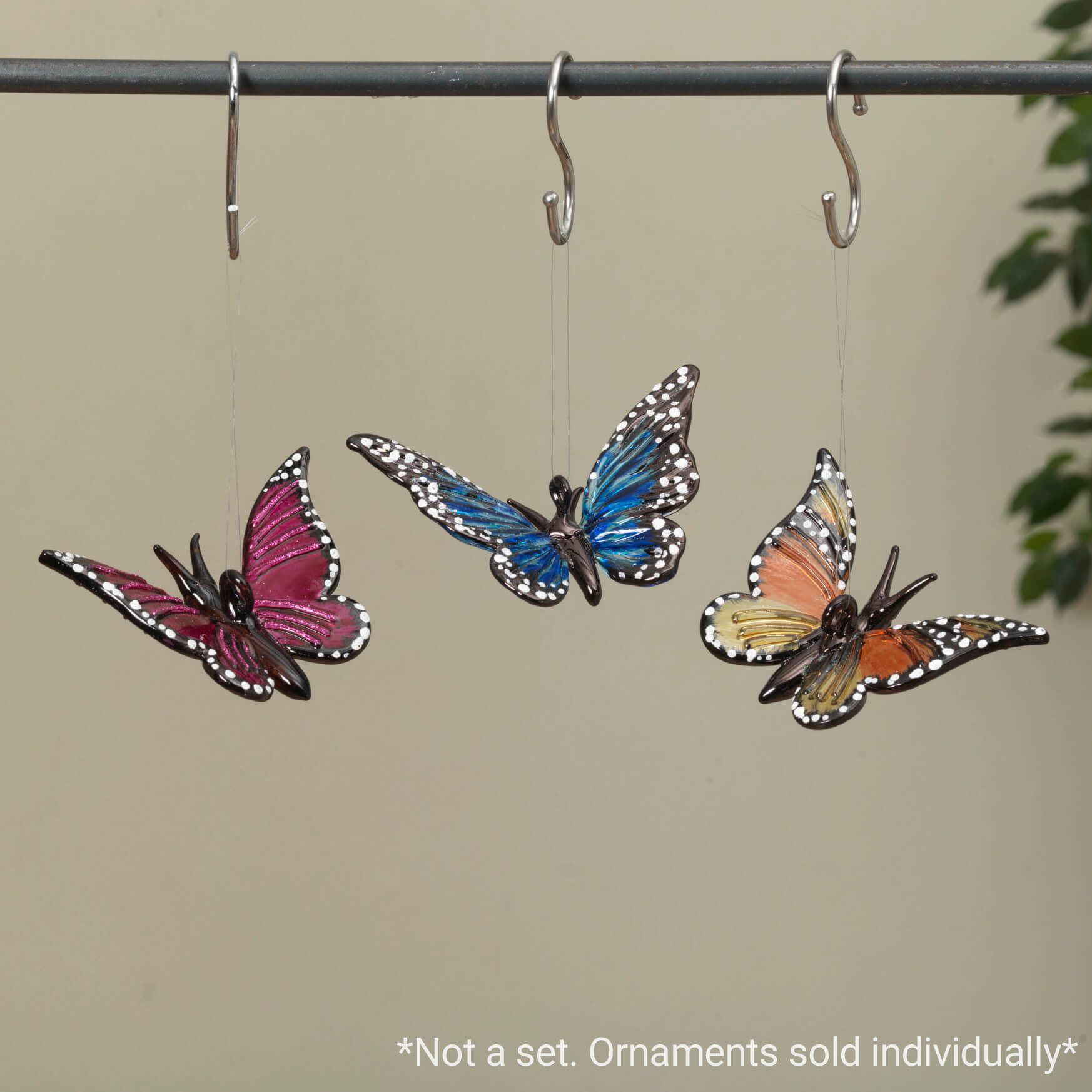 Three colorful butterfly ornaments hanging from hooks in pink, blue, and orange/yellow hues.