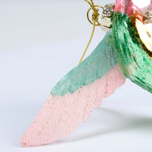 A glass hummingbird ornament with glittery pink and teal wings and a gold hanging loop perfect for decoration