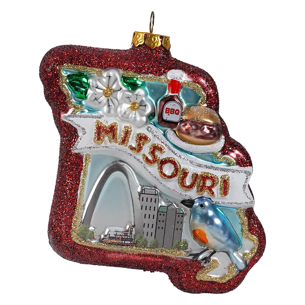 Red glittery glass missouri state ornament with white banner, gold lettering, and decorative travel and location themed details