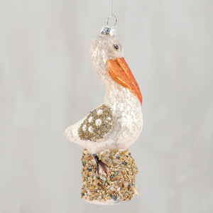 A glass pelican ornament with a glittery white body, orange beak, and pearl wings for sea and beach themed ornaments