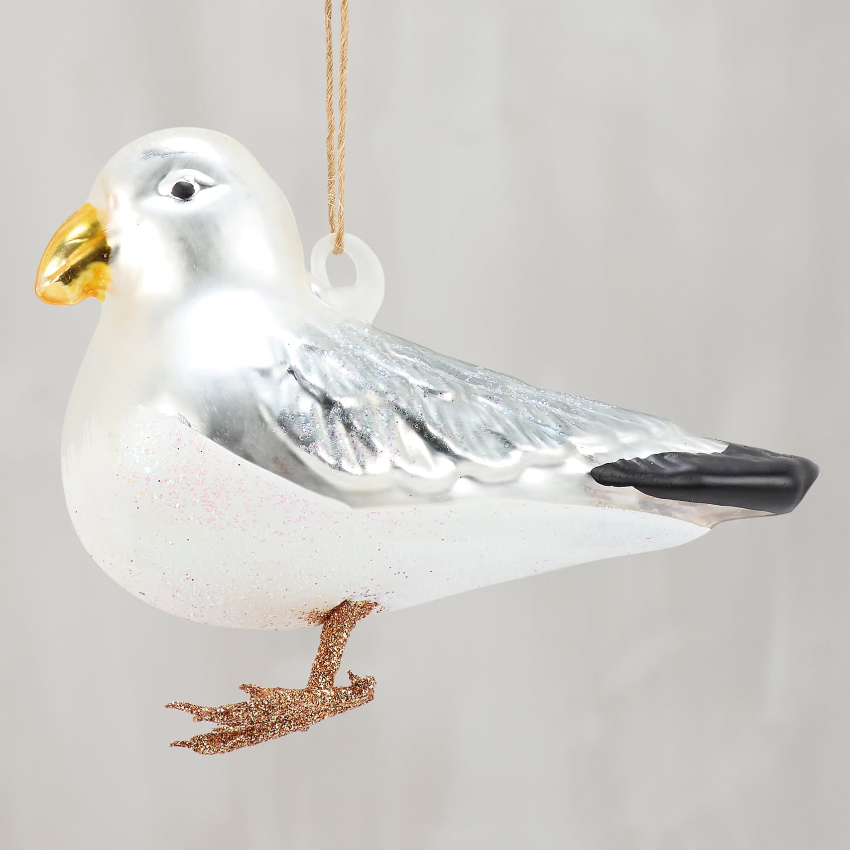 Glass seagull ornament with shiny white and silver glass, gold beak, black wing tips, and glittery bronze feet for sea and beach themed ornaments