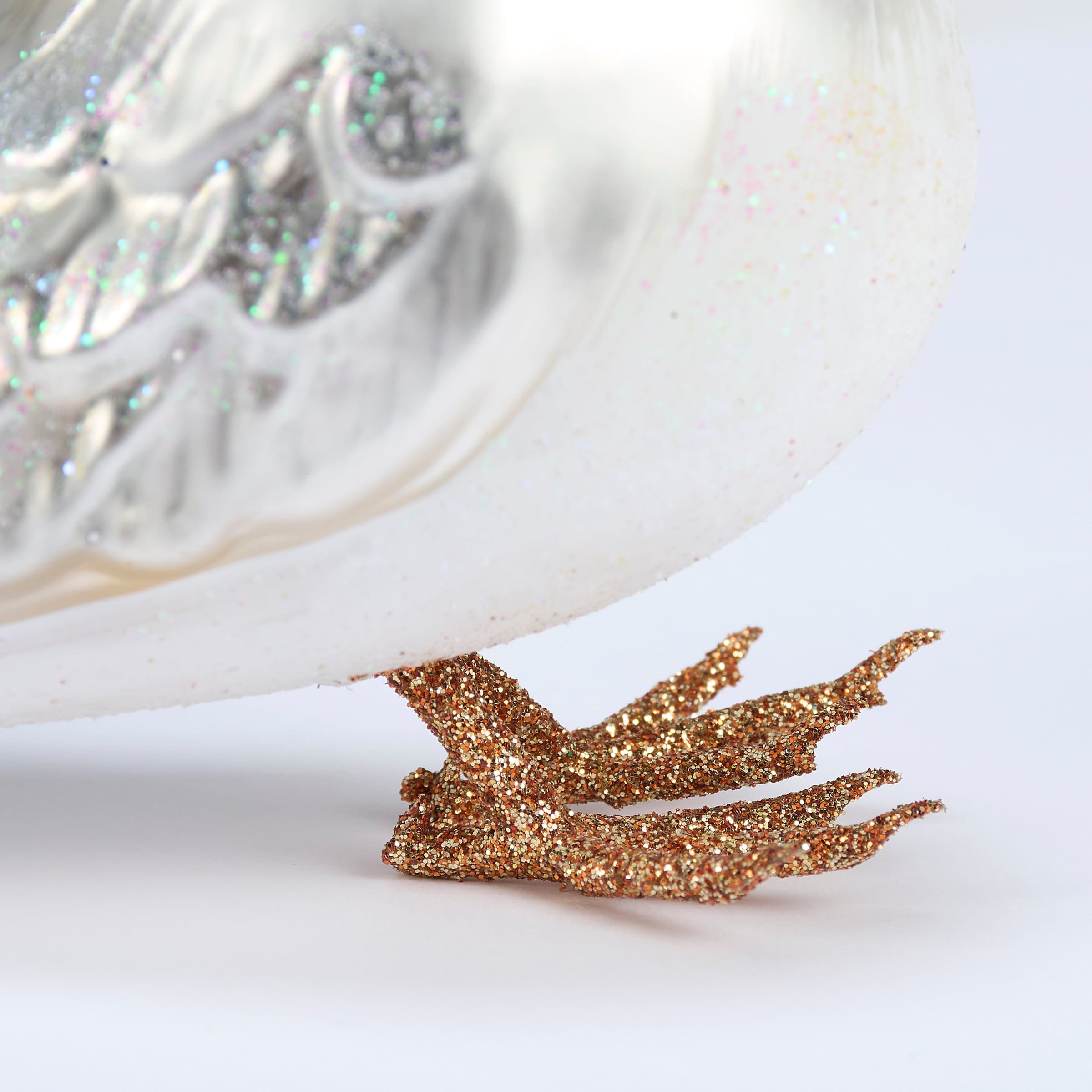 Glass seagull ornament with glittery gold feathers, translucent white body, and silver detailing for sea and beach themed ornaments